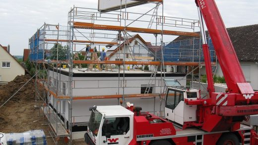 Budowa domu jednorodzinnego z żurawiem i rusztowaniami na placu budowy.