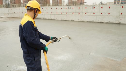 Pracownik nakłada hydroizolację na betonową powierzchnię za pomocą palnika