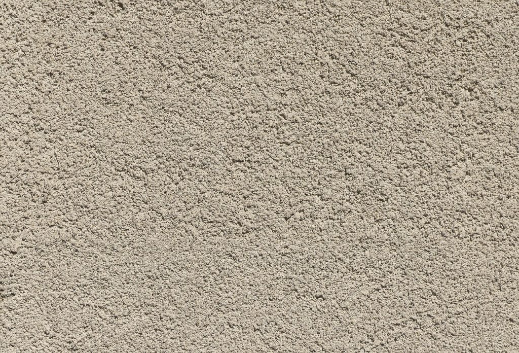 Zbliżenie na teksturę szorstkiego, mineralnego tynku ściennego w jasnym odcieniu